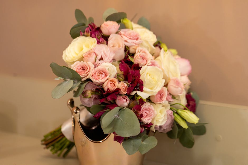 A bouquet arrangement of fresh flowers featuring soft pink roses, white roses, and deep burgundy blooms, accented with green eucalyptus leaves. The flowers are arranged in a compact, rounded style and