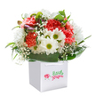 There's an uplifting charm captured in this bouquet, reflecting the tranquil cheer of Ickenham's green spaces and close-knit community. Arranged in a bright, square white gift bag, the flowers appear freshly gathered and brimming with life-lush coral and deep red carnations blooming with playful, frilled petals are joined by jubilant white daisies radiating from lime-tinged hearts. Wisps of baby's breath drift through the arrangement, illuminating it with a gentle innocence, while the entire display is cradled in a vibrant frame of broad, glossy green leaves-evocative of Ickenham's leafy vistas along Swakeleys Road. Nestled discreetly are a few purple-hued buds, hinting at the surprises and joys yet to unfold. The bag's soft handles underscore convenience for hand-delivery across the area, and the clean background ensures all attention rests on the bouquet's artful details. Designed to bring joy-be it for a milestone celebration in a local home, a thank you after a walk by the canal, or simply to brighten an autumn afternoon-this arrangement radiates sincerity and delight, a testament to the thoughtful work of an Ickenham florist.